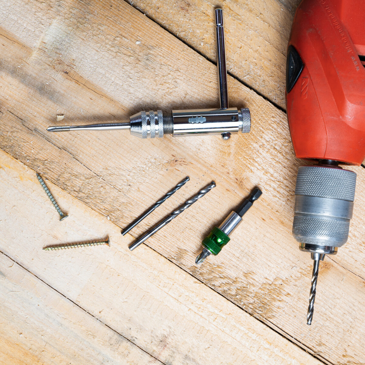 A top view of an electric drill, nails and other repairing equipments on a wooden surface